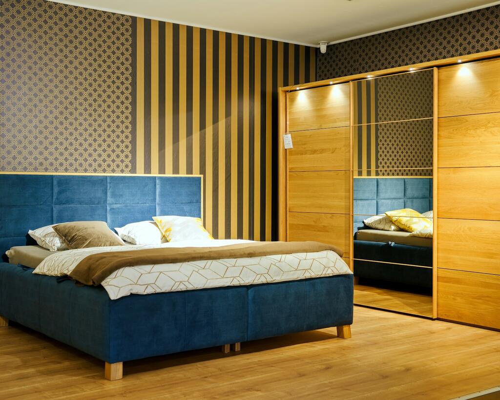Petrolblauwe velours boxspring met beige dekbedovertrek in een slaapkamer met houten kledingkast