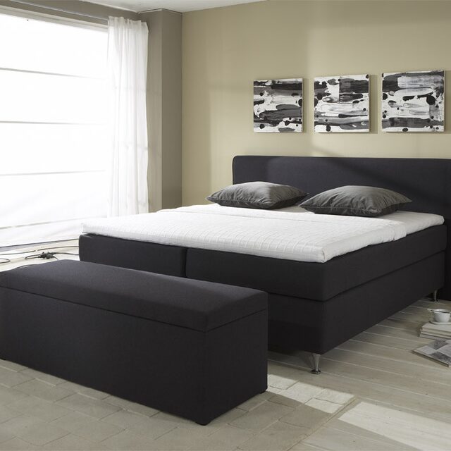 Zwarte boxspring met bijpassende hocker in een slaapkamer