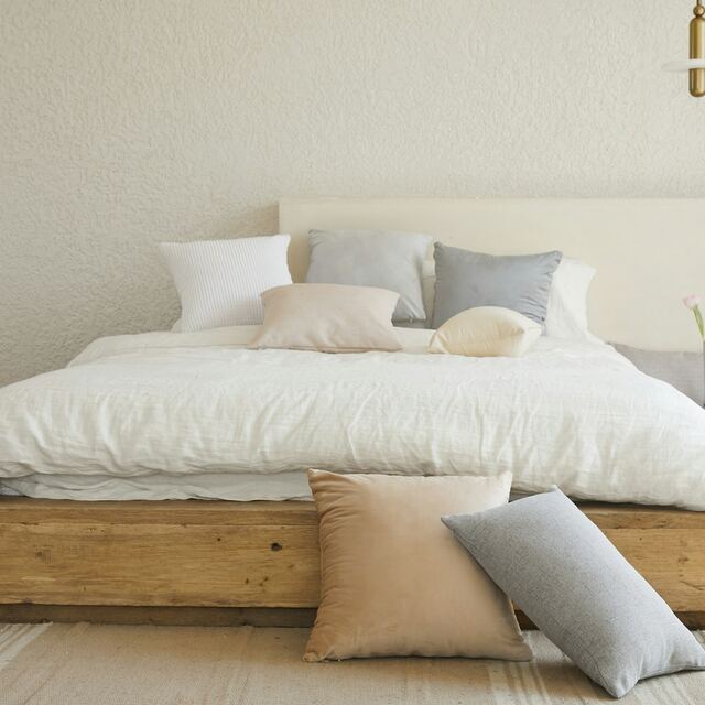 Witte, beige en grijze kussens op een houten bed met gekreukt dekbed